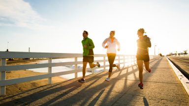 Amigos corriendo por un paseo marítimo cerca del océano Pacífico