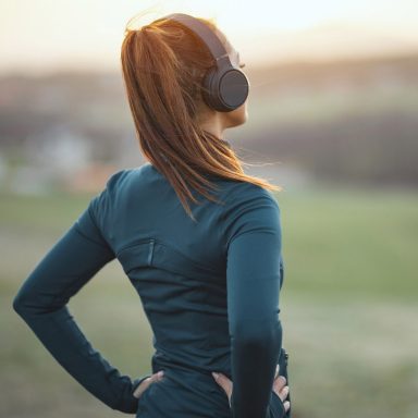 Young beautiful female runner listening to music and preparing to jogging in mountains. Rear view.