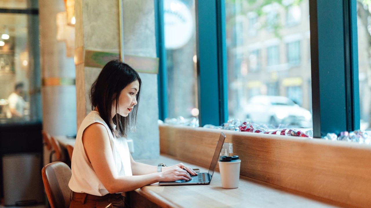 young woman working with laptop while drinking coffee at cafe