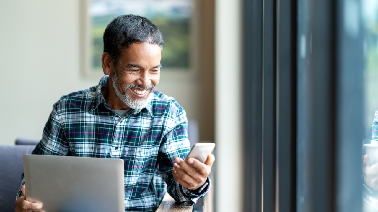 Un uomo seduto sorride al telefono con un computer portatile in grembo