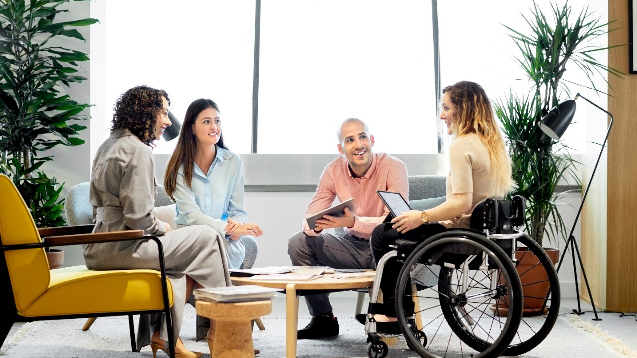 Niepełnosprawna kobieta biznesu rozmawiająca ze współpracownikami. Profesjonaliści płci męskiej i żeńskiej planujący spotkanie biznesowe. Siedzą w biurze.