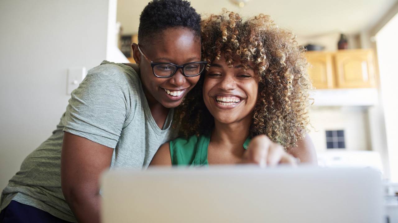 Laughing Black women hugging and using laptop