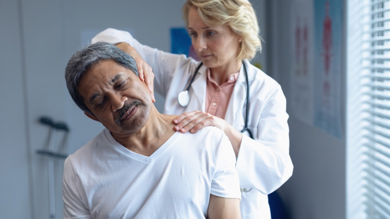 Front view of Caucasian female doctor examining mixed-race male patient neck in hospital